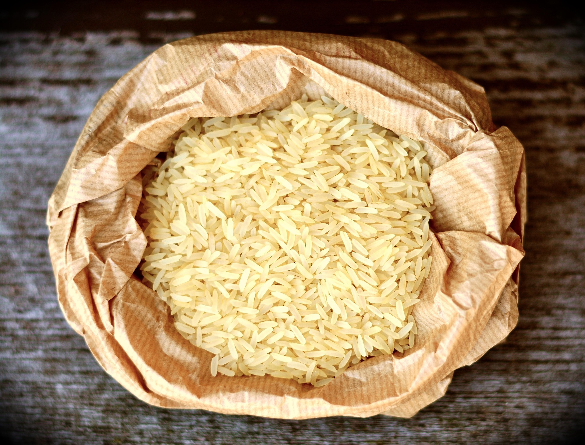 Close-up of a brown paper bag filled with uncooked rice on a wooden surface, illustrating the concept behind 'Can I Use Rice as Cat Litter?' by showcasing rice's texture and absorbency as a potential litter alternative.