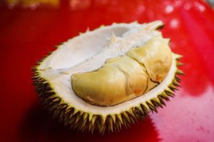 Open durian fruit with creamy yellow flesh on a red surface, raising the question: can cats eat durian? The spiky shell and pungent aroma highlight why this tropical fruit sparks curiosity among cat owners exploring feline-safe foods.