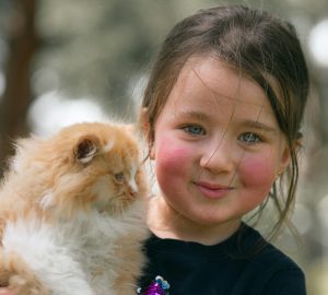 A smiling child with blue eyes gently holds a fluffy orange kitten outdoors, illustrating warmth and companionship. This tender moment highlights themes of innocence and answers the question, Are Persian Cats Good With Children And Other Pets, by showing the gentle bond between kids and animals in a family‑friendly setting.